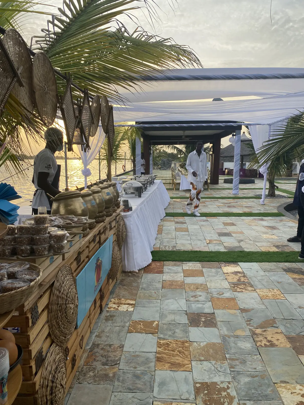 A buffet station under palm-thatched shades by the water